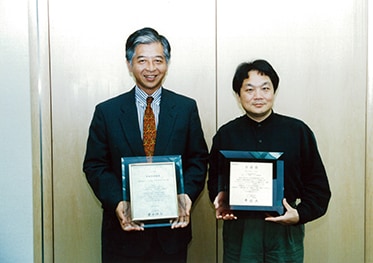 Teruhisa Tokunaka (chapda) va Ken Kutaragi — Ibuka mukofoti bilan